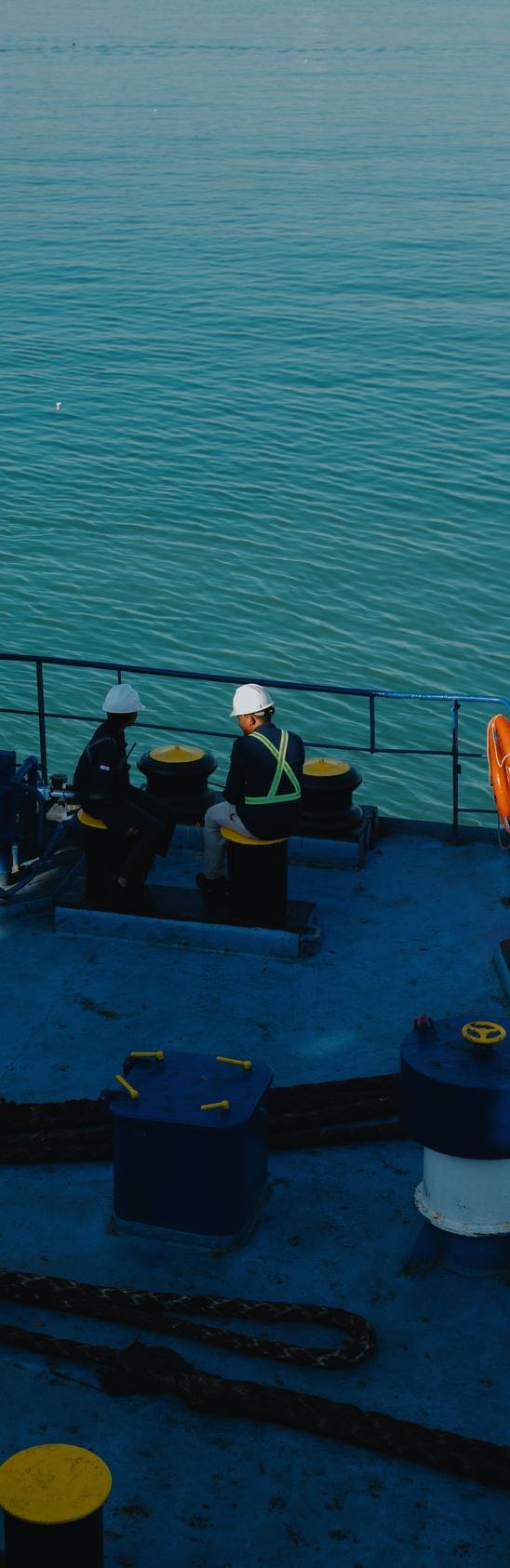 Tripulantes con casco conversando junto a la borda de un buque en el muelle